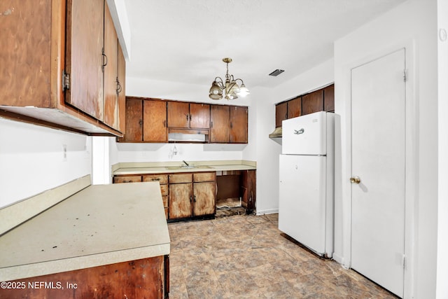 kitchen with an inviting chandelier, freestanding refrigerator, light countertops, stone finish flooring, and visible vents