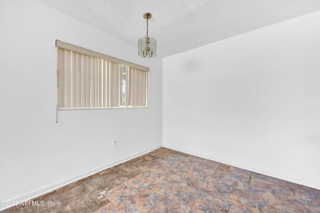 unfurnished room featuring a chandelier, baseboards, stone finish flooring, and a textured ceiling