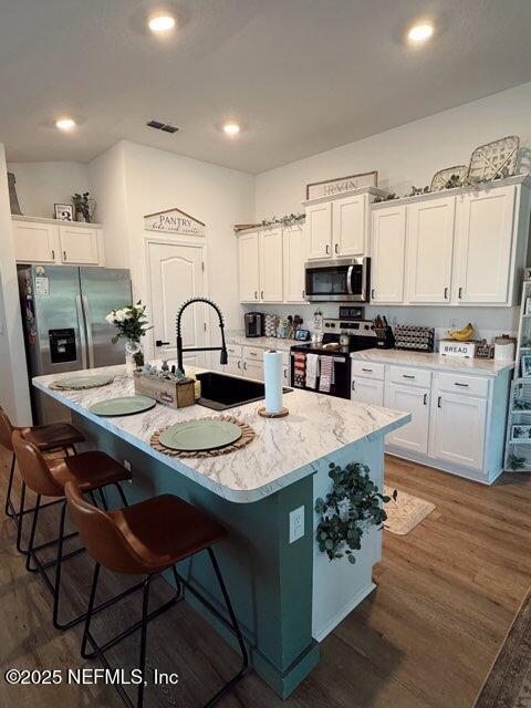 kitchen with dark wood finished floors, appliances with stainless steel finishes, a sink, white cabinetry, and visible vents