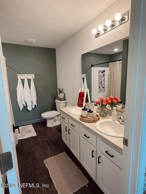 full bath with wood finished floors, a textured ceiling, double vanity, and a sink
