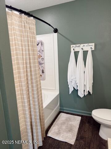 bathroom featuring toilet, shower / bath combo with shower curtain, wood finished floors, and baseboards