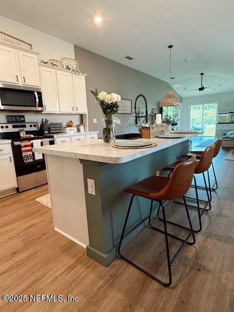 kitchen featuring white cabinetry, stainless steel appliances, an island with sink, and light wood finished floors