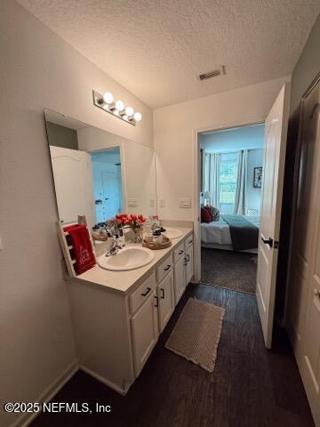 bathroom with a textured ceiling, a sink, double vanity, ensuite bathroom, and wood finished floors
