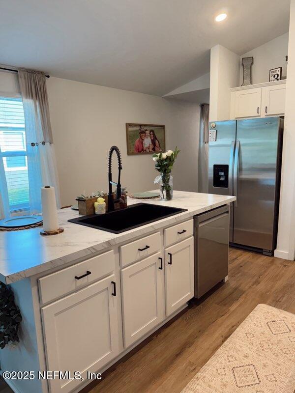 kitchen featuring stainless steel appliances, vaulted ceiling, light wood finished floors, a sink, and white cabinetry