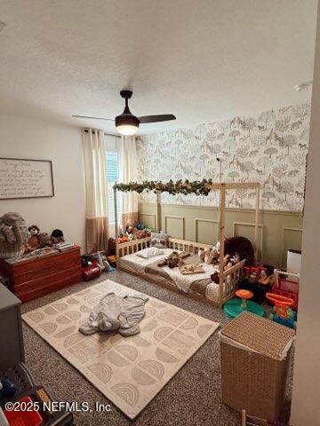 bedroom with a wainscoted wall, carpet, and a textured ceiling