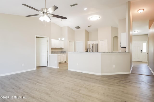 unfurnished living room with light wood-type flooring, ceiling fan with notable chandelier, baseboards, visible vents, and high vaulted ceiling