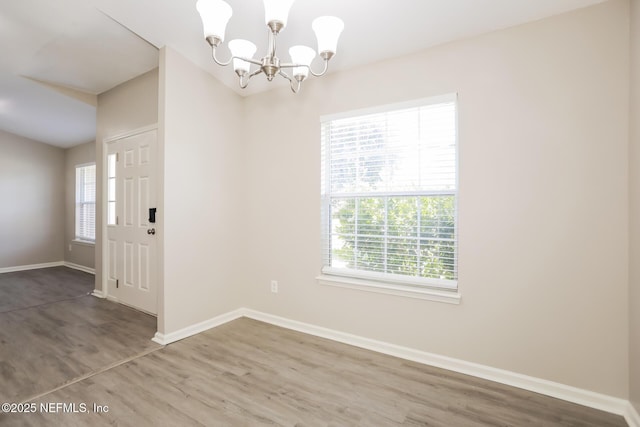 unfurnished dining area featuring baseboards, wood finished floors, and a notable chandelier