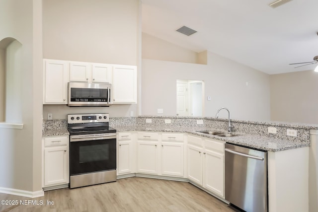 kitchen with appliances with stainless steel finishes, vaulted ceiling, a sink, light wood-type flooring, and a peninsula
