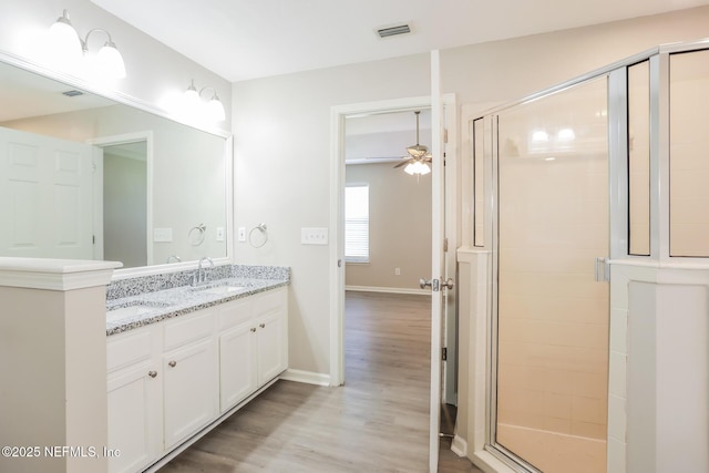 bathroom with wood finished floors, ceiling fan, a sink, visible vents, and a stall shower