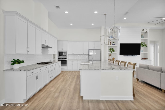kitchen featuring stainless steel appliances, a sink, open floor plan, under cabinet range hood, and white cabinetry
