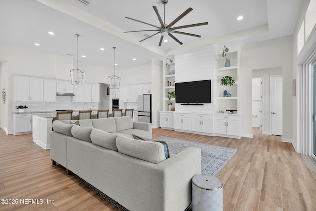 living area featuring a high ceiling, light wood finished floors, a ceiling fan, and recessed lighting