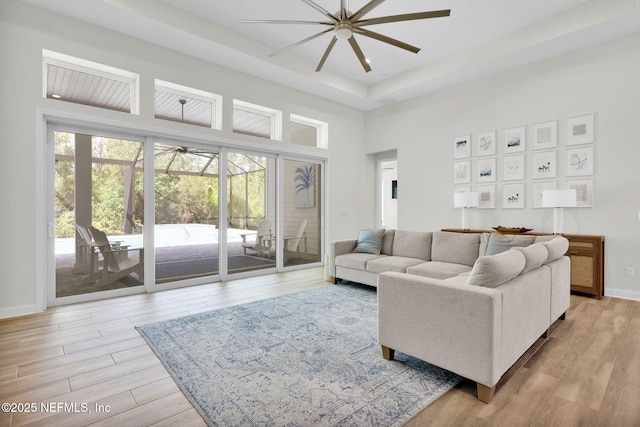 living area with baseboards, a ceiling fan, light wood-style flooring, and a tray ceiling