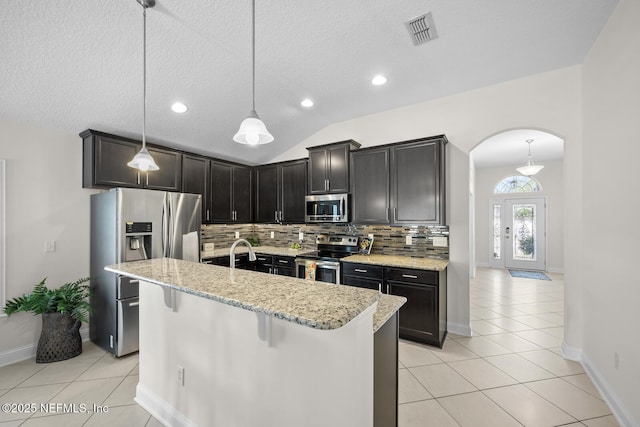 kitchen featuring appliances with stainless steel finishes, light stone counters, arched walkways, decorative backsplash, and light tile patterned floors