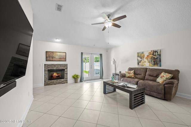 living room featuring ceiling fan, french doors, a stone fireplace, visible vents, and baseboards