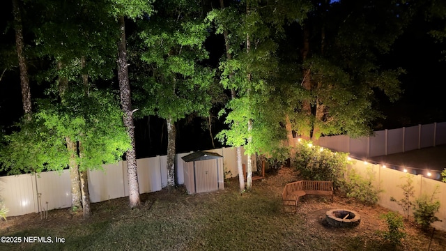 view of yard featuring a storage unit, a fenced backyard, an outdoor fire pit, and an outdoor structure