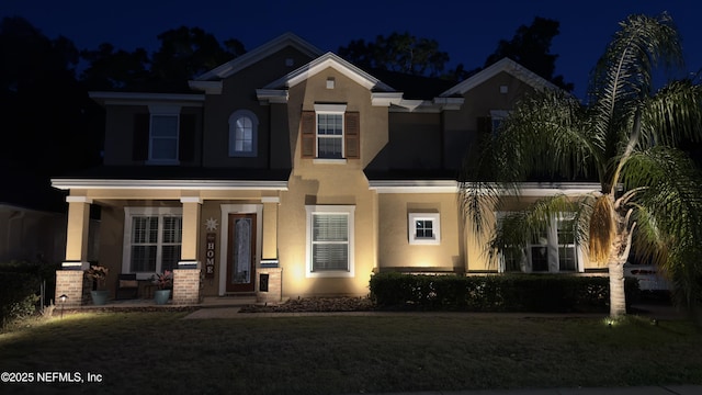 view of front facade featuring covered porch, a yard, and stucco siding