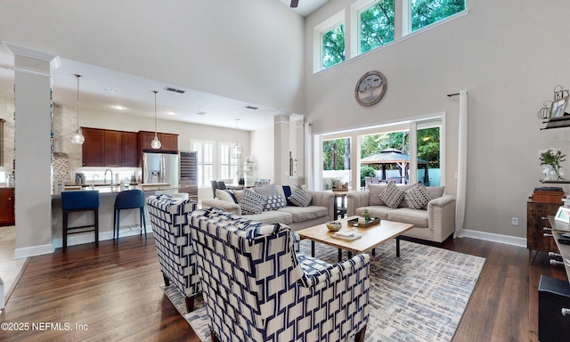 living room featuring a healthy amount of sunlight, a high ceiling, decorative columns, and dark wood-style flooring