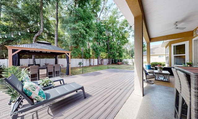 deck with a gazebo, a fenced backyard, ceiling fan, and outdoor dining space