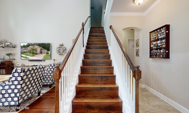 stairway with crown molding, arched walkways, baseboards, and tile patterned floors
