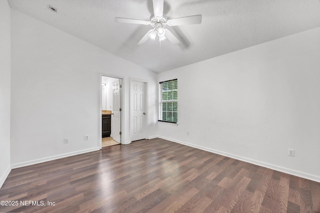 unfurnished bedroom featuring dark wood-type flooring, connected bathroom, baseboards, and vaulted ceiling