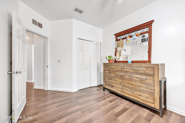 bedroom featuring baseboards, a closet, wood finished floors, and visible vents
