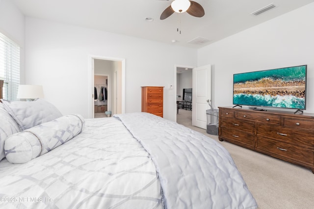 bedroom with ceiling fan, visible vents, light carpet, and a walk in closet