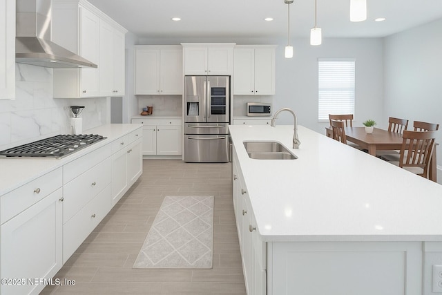 kitchen with decorative backsplash, an island with sink, wall chimney exhaust hood, a sink, and appliances with stainless steel finishes