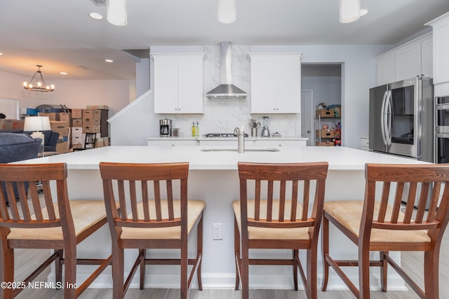 kitchen featuring decorative backsplash, wall chimney exhaust hood, light countertops, a sink, and white cabinetry