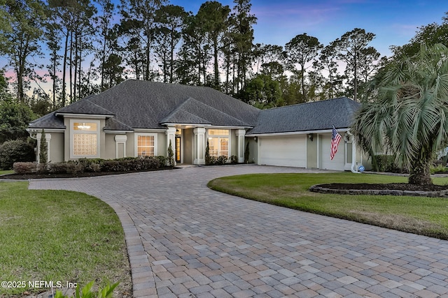 view of front of home featuring stucco siding, a garage, curved driveway, and a front lawn