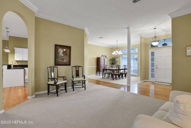living area with an inviting chandelier, light carpet, arched walkways, baseboards, and ornamental molding