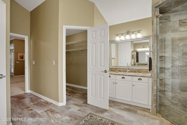 bathroom with vanity, a walk in closet, vaulted ceiling, and tiled shower