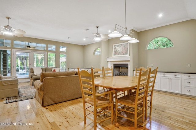 dining room featuring a tiled fireplace, light wood-style floors, ceiling fan, and a wealth of natural light