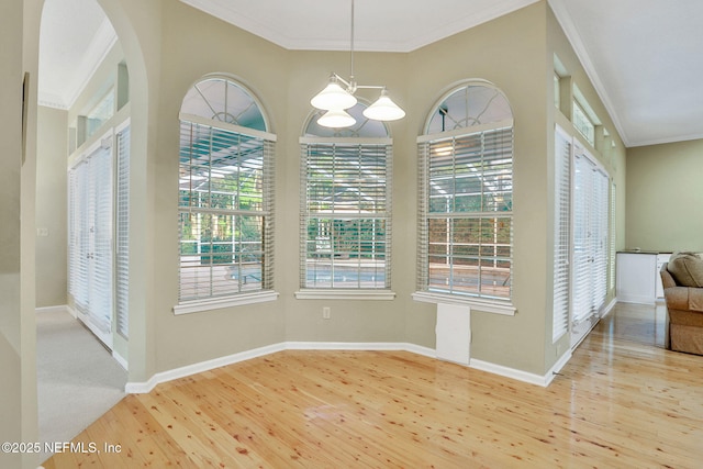 unfurnished dining area with baseboards, ornamental molding, wood finished floors, and a notable chandelier