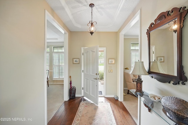 foyer with a textured ceiling, hardwood / wood-style floors, baseboards, and a tray ceiling