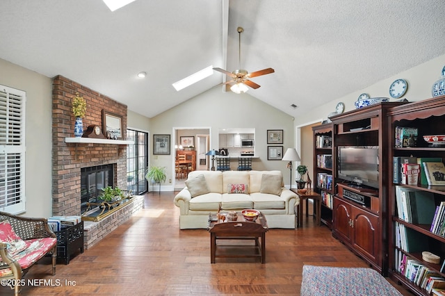 living room with a fireplace, dark wood-style flooring, a ceiling fan, and lofted ceiling with skylight