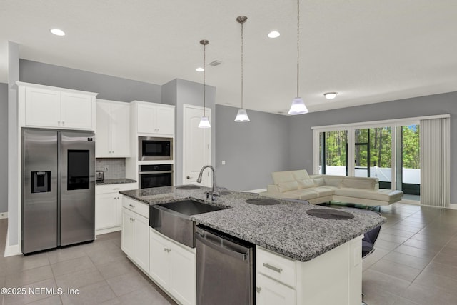 kitchen featuring a center island with sink, a sink, light tile patterned floors, open floor plan, and stainless steel appliances