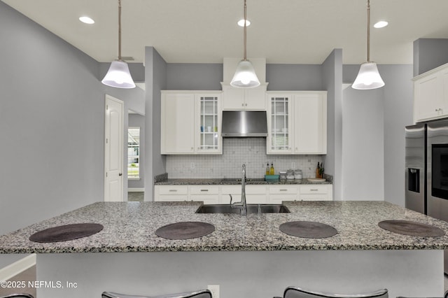 kitchen featuring a breakfast bar area, tasteful backsplash, a sink, stainless steel fridge with ice dispenser, and under cabinet range hood