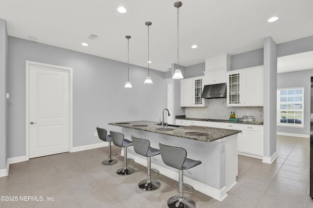 kitchen with decorative backsplash, a sink, glass insert cabinets, dark stone counters, and under cabinet range hood