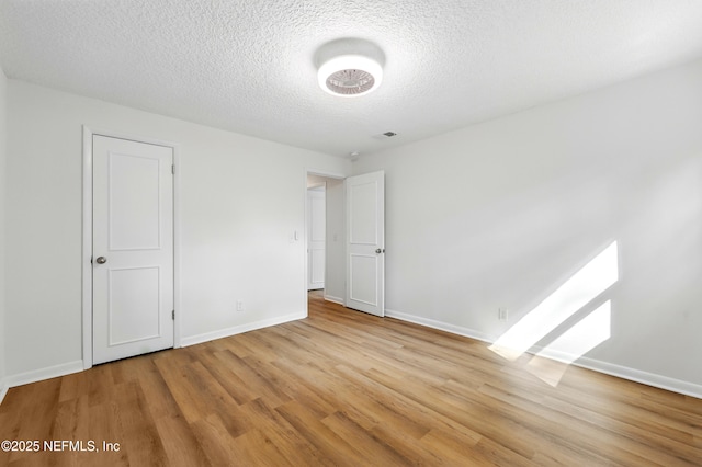 unfurnished bedroom featuring a textured ceiling, baseboards, and light wood-style floors