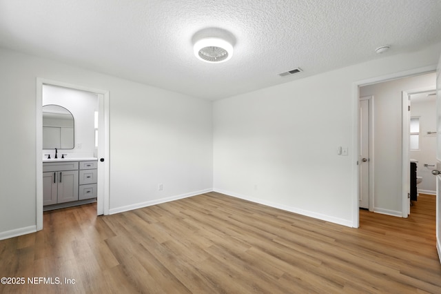 unfurnished bedroom with visible vents, baseboards, a textured ceiling, a sink, and light wood-style flooring