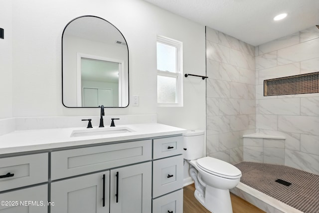 full bathroom with vanity, wood finished floors, toilet, recessed lighting, and a tile shower