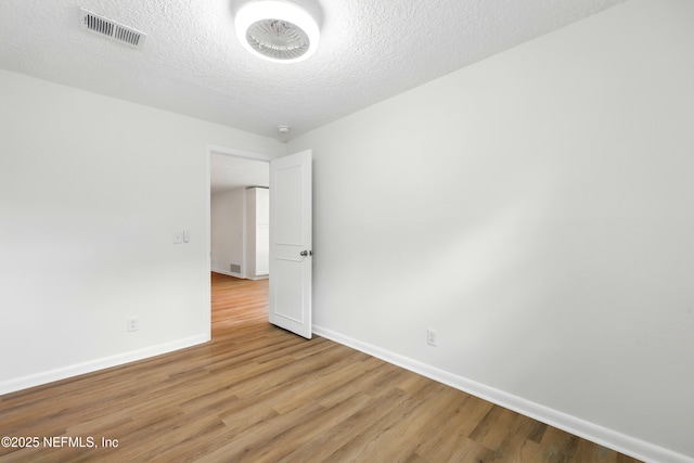 empty room with light wood-style floors, baseboards, a textured ceiling, and visible vents