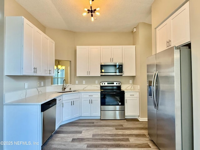 12359 Silent Brook Trl N, Jacksonville, FL 32225 - kitchen featuring a textured ceiling, light wood-style flooring, a sink, stainless steel appliances, and an inviting chandelier