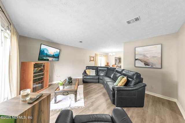 living room with a textured ceiling, visible vents, wood finished floors, baseboards, and a chandelier