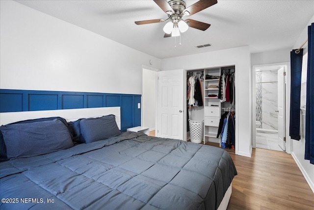 bedroom with a closet, ensuite bath, a ceiling fan, visible vents, and wood finished floors