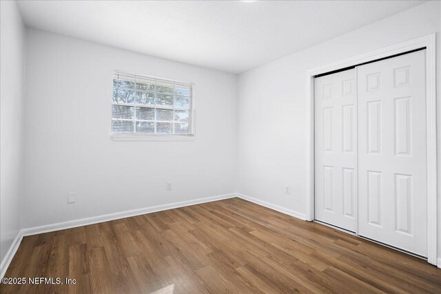 unfurnished bedroom with baseboards, wood finished floors, and a closet
