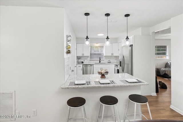 kitchen with appliances with stainless steel finishes, backsplash, a sink, dark wood-style floors, and a peninsula