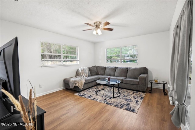 living area featuring a ceiling fan, a textured ceiling, wood finished floors, and baseboards