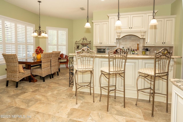 3771 Saltmeadow Ct S, Jacksonville, FL 32224 - kitchen with tasteful backsplash, light stone counters, hanging light fixtures, a kitchen bar, and a chandelier
