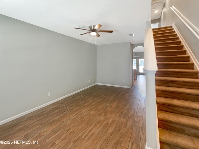 interior space featuring wood finished floors, arched walkways, baseboards, stairway, and a ceiling fan